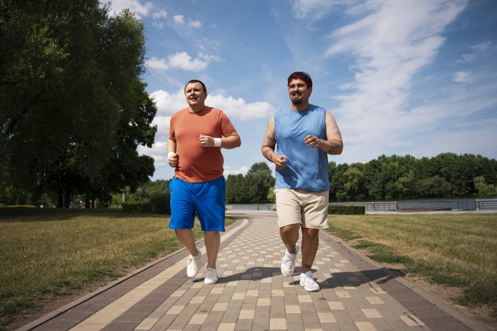 Dois homens sorridentes correndo em parque ao ar livre, promovendo hábitos saudáveis.