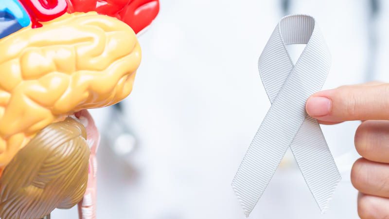 Pessoa segurando um modelo anatômico de cérebro humano e uma fita cinza, símbolo da campanha Maio Cinza.