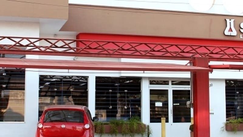 Fachada do laboratório médico Sancet com letreiro e carro vermelho estacionado em frente.