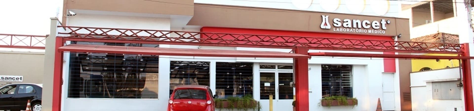 Fachada do laboratório médico Sancet com letreiro e carro vermelho estacionado em frente.
