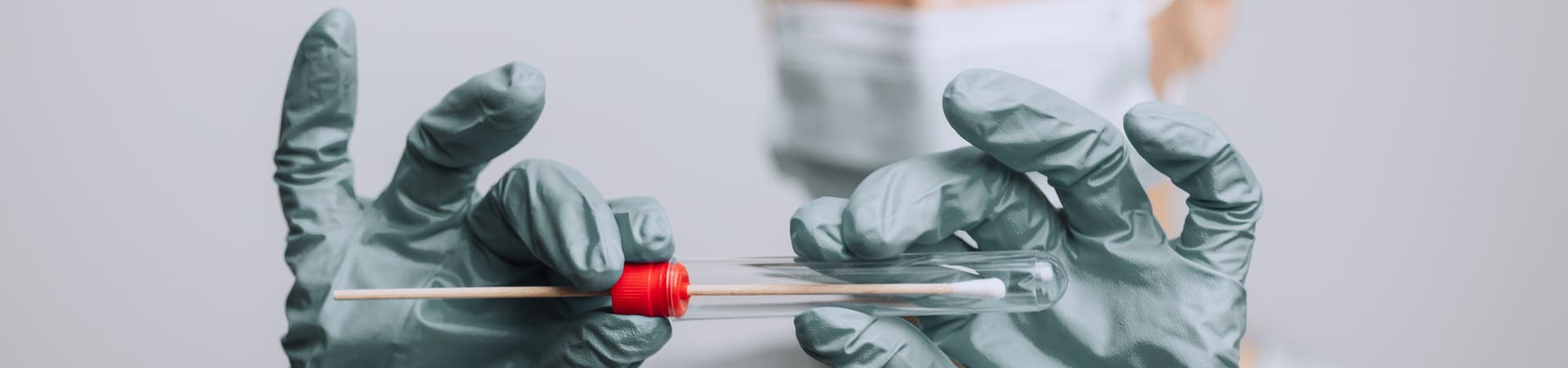Profissional de saúde com luvas segura um tubo de coleta contendo um swab para exame de painel viral respiratório.