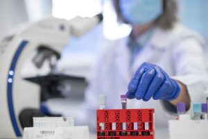 Profissional de laboratório com luvas azuis manipula tubos de ensaio em bancada durante a análise de exames genéticos.