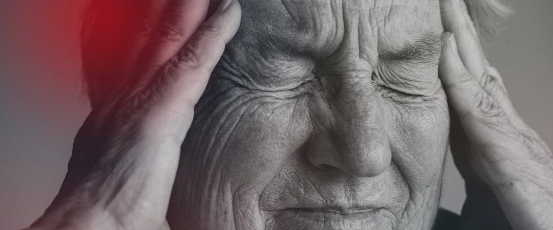 Pessoa idosa com expressão de dor e mãos na cabeça, representando os primeiros sinais de AVC.