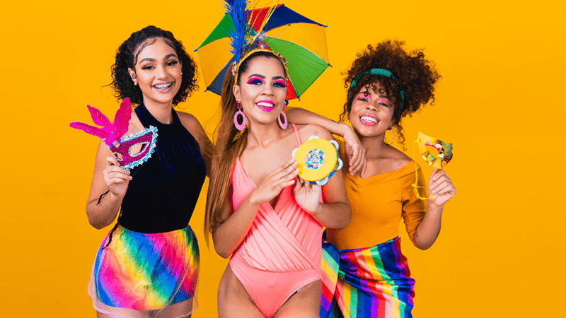 Grupo de amigas fantasiadas celebrando o carnaval com alegria e cores vibrantes, representando diversão com saúde e segurança.