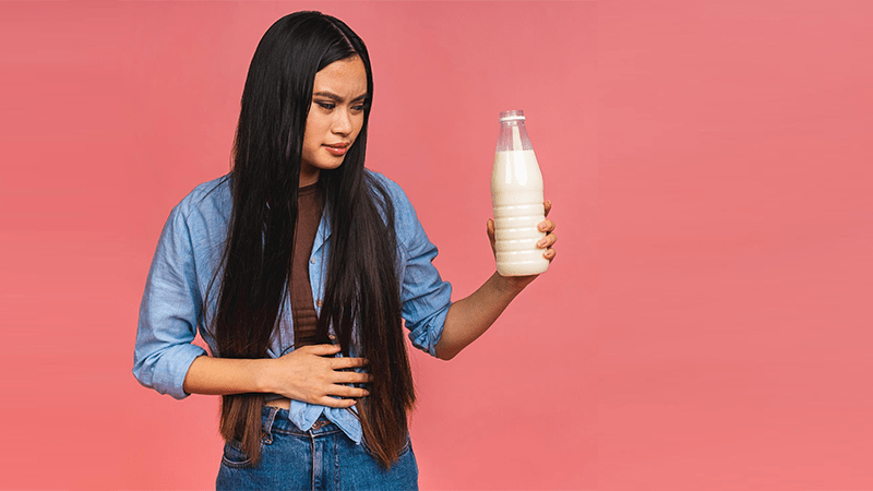 Mulher segurando uma garrafa de leite com expressão de desconforto abdominal, ilustrando os sintomas da intolerância à lactose.