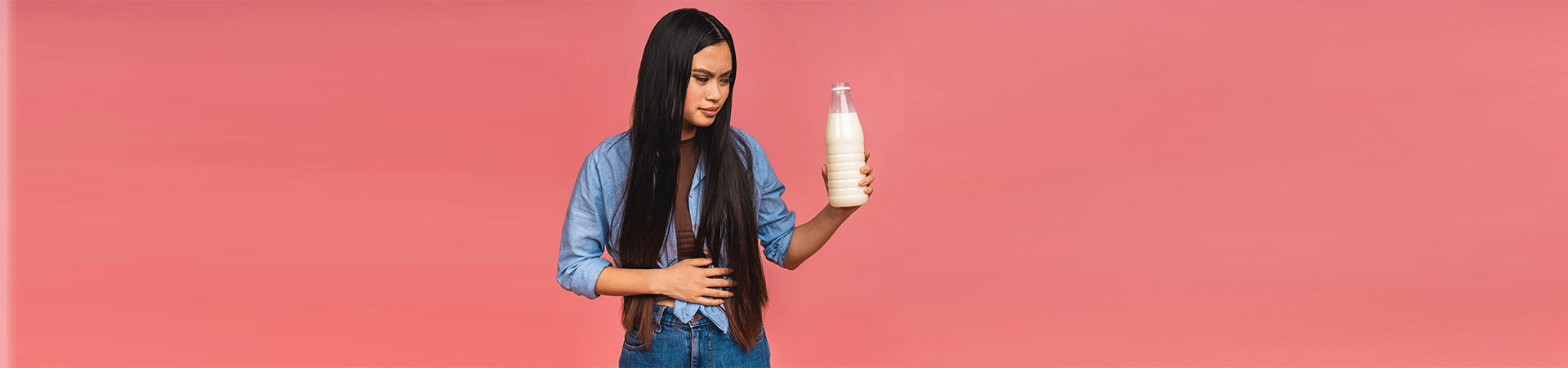 Mulher segurando uma garrafa de leite com expressão de desconforto abdominal, ilustrando os sintomas da intolerância à lactose.