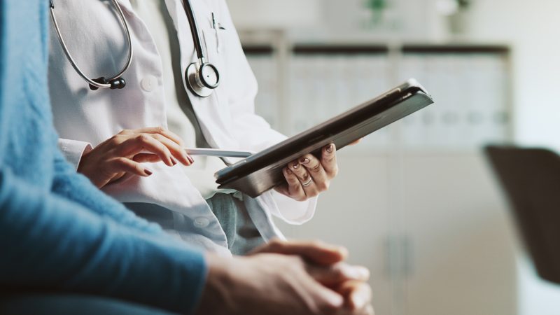 Profissional de saúde utilizando tablet durante consulta, organizando exames laboratoriais com agendamento para facilitar o acompanhamento da saúde.