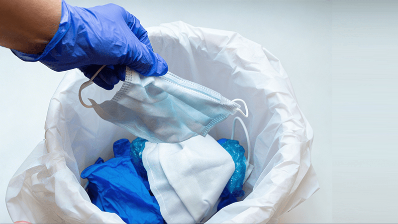 Profissional com luvas descartando máscara e resíduos em lixeira, representando práticas de descarte responsável no dia internacional do lixo.