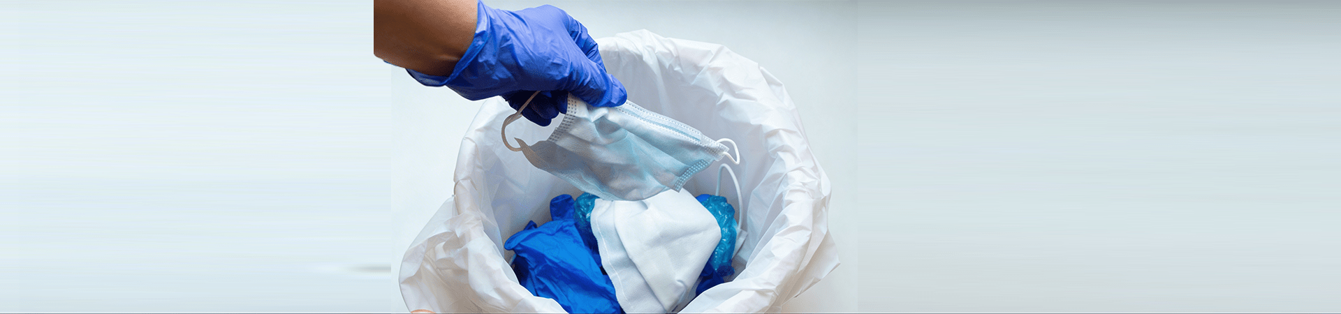 Profissional com luvas descartando máscara e resíduos em lixeira, representando práticas de descarte responsável no dia internacional do lixo.