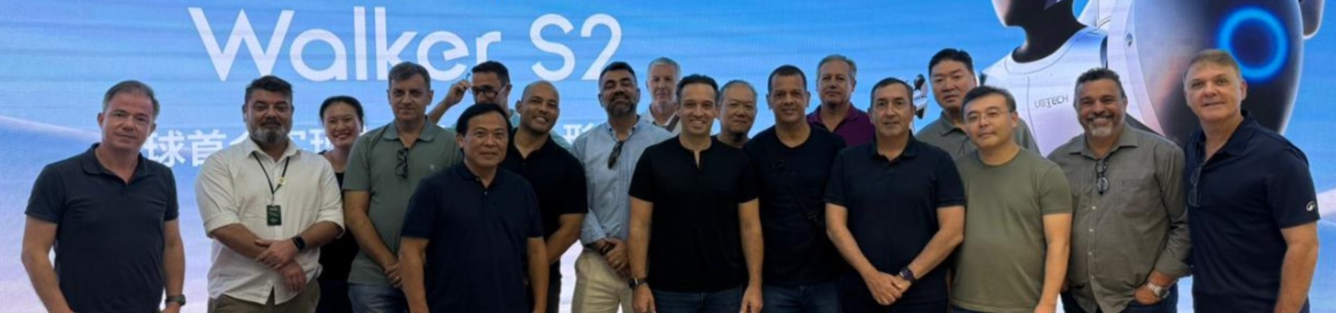 Grupo de profissionais reunidos em evento corporativo internacional diante de painel tecnológico Walker S2.