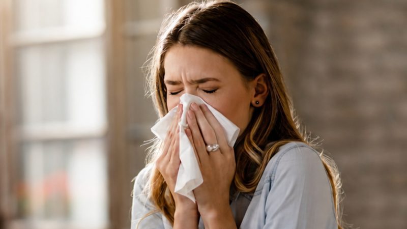 Mulher espirrando em um lenço enquanto apresenta sintomas respiratórios.