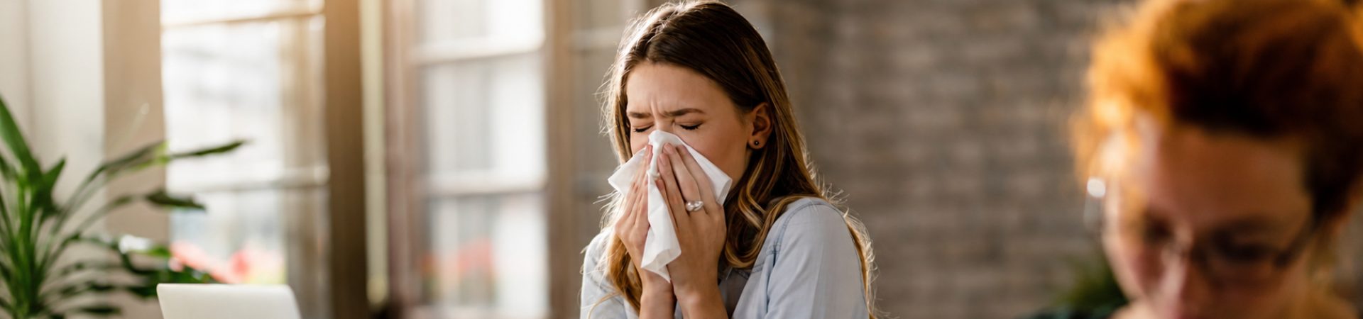 Mulher espirrando em um lenço enquanto apresenta sintomas respiratórios.