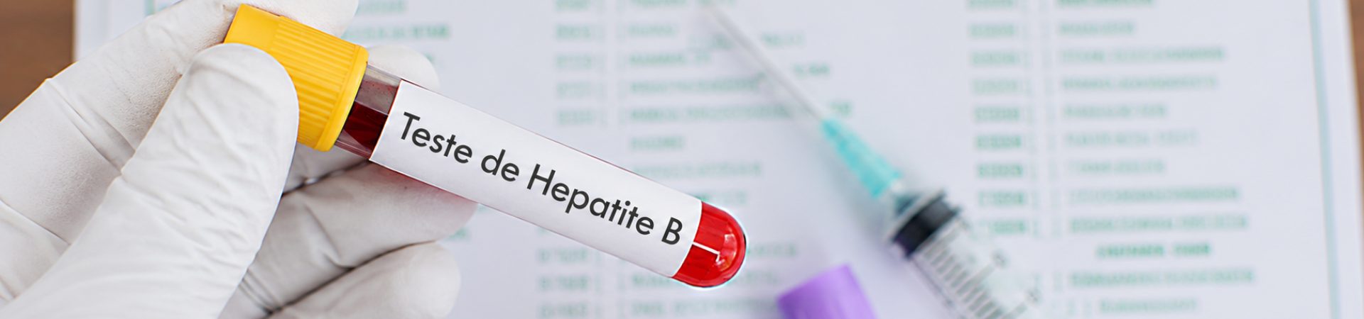 Tubo de coleta de sangue identificado para teste de Hepatite B ao lado de uma seringa.