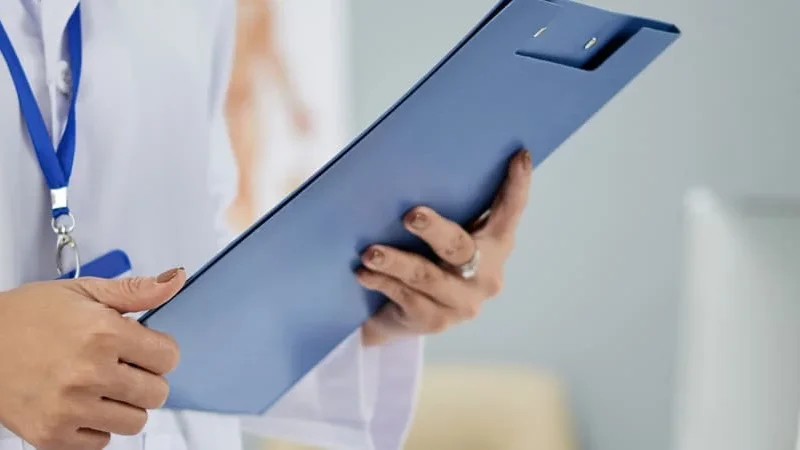 Médica segurando prancheta durante consulta com paciente para discutir os resultados de seus exames de função hepática.